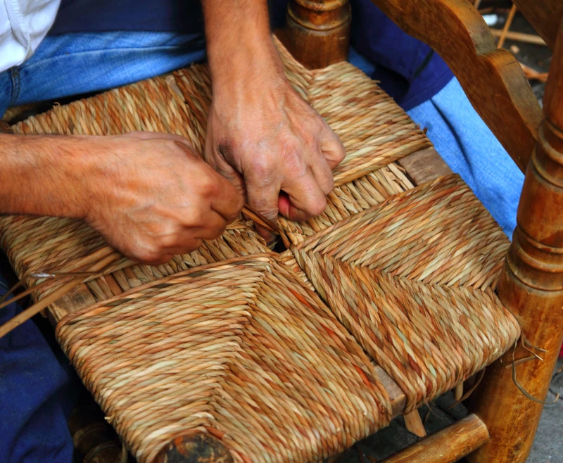 Mains d'artisan en train de rempailler une chaise ancienne